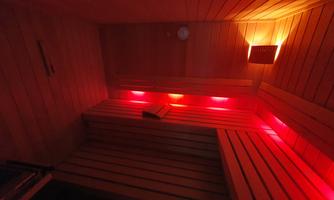 A modern sauna with wooden benches and atmospheric red lighting. The room feels inviting and relaxing.