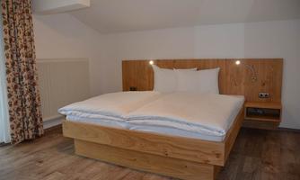 A cozy bedroom with a wooden bed and white bedcovers. Curtains with a floral pattern hang on the wall.