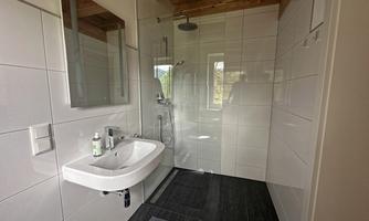 A modern bathroom with a shower and a sink. White walls and wooden details create a bright, inviting atmosphere.