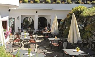 A cozy restaurant with outdoor tables and umbrellas. The surroundings are green and inviting.