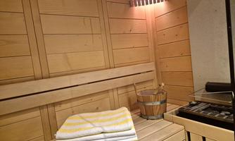A cozy sauna area with a wooden bench and towels. Next to the bench stands a bucket and a sauna stove.