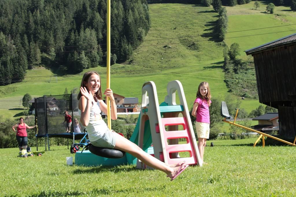 Children are playing in a playground in a beautiful, green landscape. A girl is swinging on a swing and smiling.