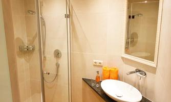 A modern bathroom with a shower and a large, round sink. There are orange towels next to the sink and a mirror on the wall.
