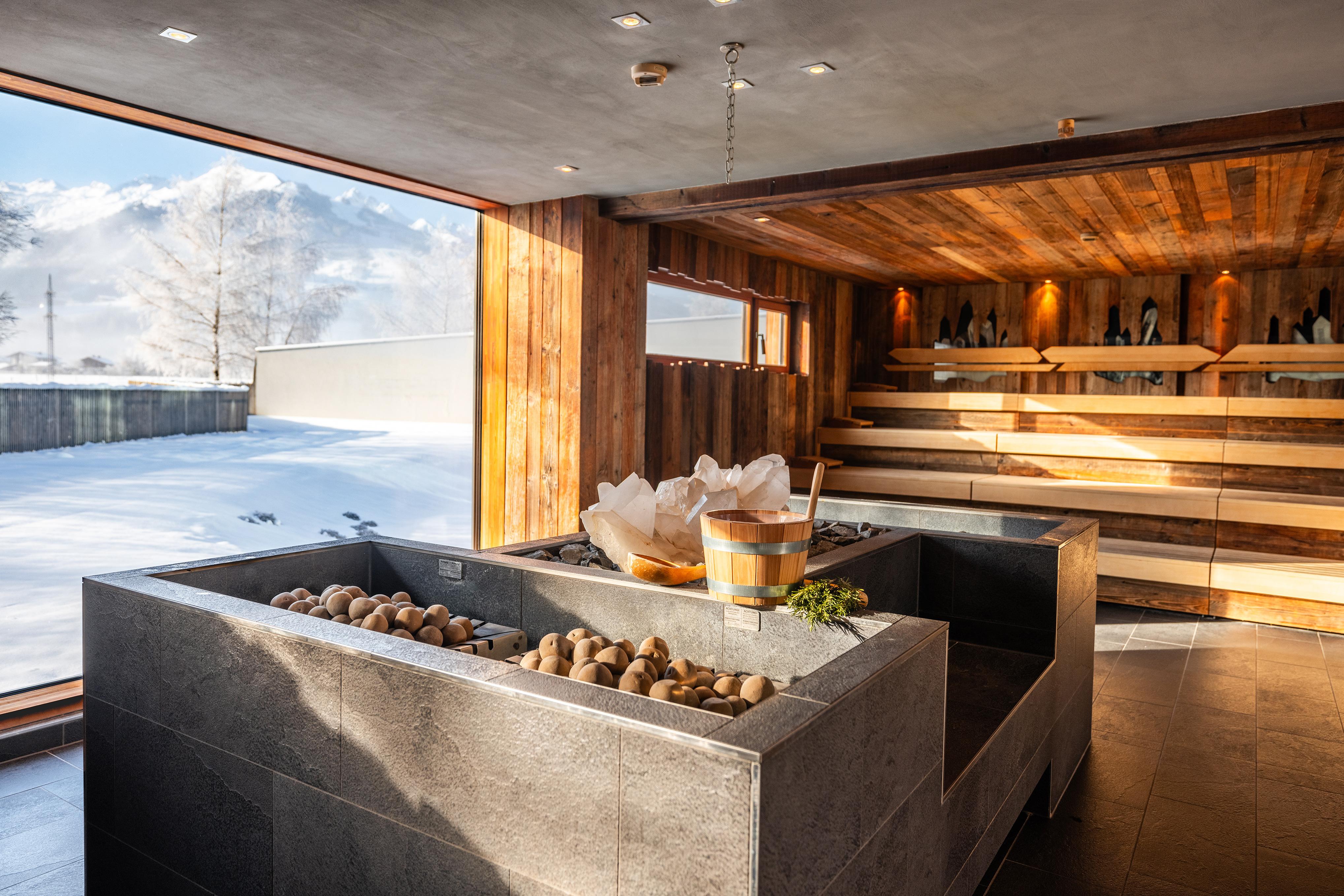 A modern wellness area with an elegant stone trough and large windows that offer a view of the snowy landscape. The wooden interior creates a cozy atmosphere.