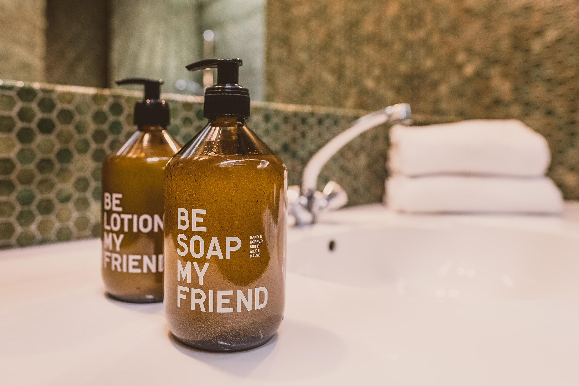 Two bottles of soap and lotion are sitting on a sink. In the background, towels are visible, and the wall has a green tile covering.