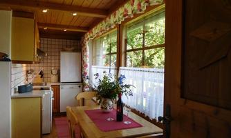 A cozy kitchen with a wooden ceiling and large windows. On the table, there are flowers and a bottle of wine.