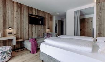 A modern room with wooden paneling and elegant furnishings. There is a comfortable bed, a couch, and a flat-screen TV.