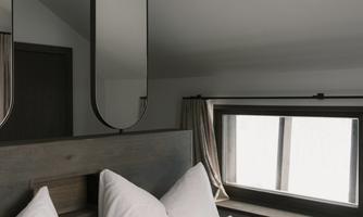 A modern bedroom with a large window and stylish mirrors. The beds are decorated with white pillows and blankets.
