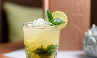 A refreshing cocktail with mint and lime in a glass. In the background, a stylish bar setting can be seen.