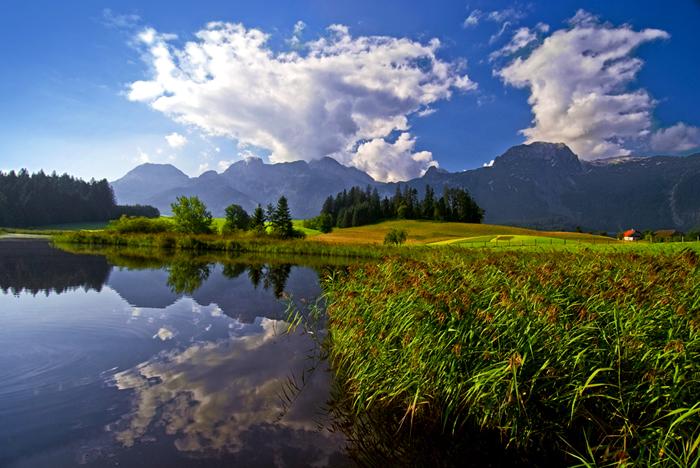 A beautiful lake with green meadows and mountains in the background. Soft clouds reflect in the clear water.