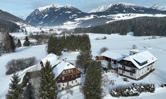 A picturesque winter landscape with snow-covered mountains and traditional alpine houses. The scene is calm and peaceful, surrounded by coniferous trees.