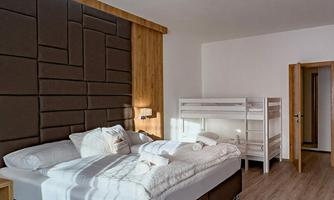 A modern bedroom with a large double bed and a bunk bed. The walls are light and designed in a minimalist style.