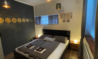 A modern bedroom with a cozy bed and decorative pillows. The walls are designed in soft colors, and there are stylish lamps as well as picture frames.