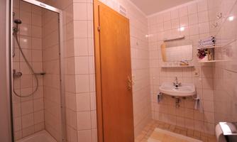 A simple bathroom with a shower, a sink, and a wooden cabinet. The walls are tiled with light tiles.