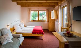 A cozy room with two beds and a modern television. Large windows provide plenty of daylight and a view of nature.