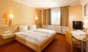 A bright hotel room with two single beds, wooden furniture, and a desk. Curtains in soft colors hang at the window, and the walls are designed in warm tones.
