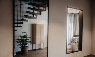A modern interior with a wooden staircase and a stylish wardrobe. In the background, curtains and a plant are visible.