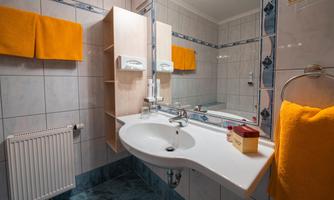 A modern bathroom with a sink and a large mirror. Orange towels and a bright tiled wall give the room a fresh touch.