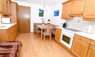 A bright kitchen with wooden furniture and a dining table for four people. The facilities include a stove, a microwave, and a refrigerator.