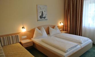 A cozy hotel room with two beds and modern furnishings. The room has warm colors and plenty of daylight from a large window.