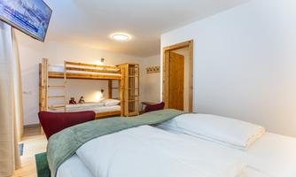 A modern bedroom with a double bed and a bunk bed. The decor is bright and cheerful, with a television and a cozy armchair.