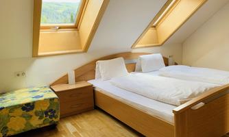 A cozy bedroom with two beds, wooden floor, and large skylights. The decor is modern and bright, with a colorful nightstand.