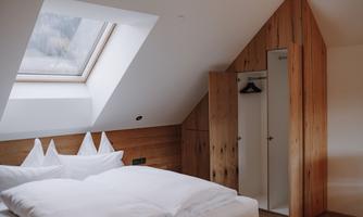 A cozy bedroom with wooden paneling and a large skylight. The bed is furnished with white pillows and blankets.