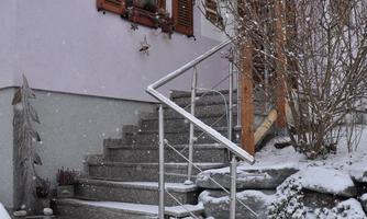 A cozy house with an entrance and a snowy staircase. The windows are adorned with wooden beams and light snow is falling.