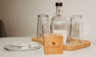 A stylish set with glasses, a carafe, and a wooden block inscribed with "Lökerwirt". Additionally, some small packages are placed on a plate.