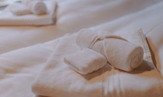 Clean, white towels are placed on a bed. A folded towel and a washcloth are also neatly arranged.