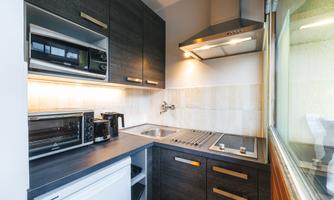 A kitchen with dark cabinets and stainless steel appliances. It is bright and compact, with a window that lets light in.