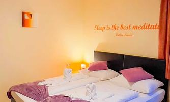 A cozy bedroom with two beds, decorated with a purple blanket. On the wall is the saying "Sleep is the best meditation."