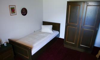 A simple bedroom with a single bed and a wooden wardrobe. On the wall hangs a picture and a round clock.