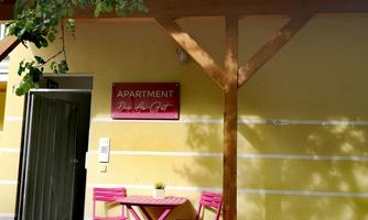An apartment with an inviting entrance. Outside, there is a small pink table and chairs, surrounded by greenery.