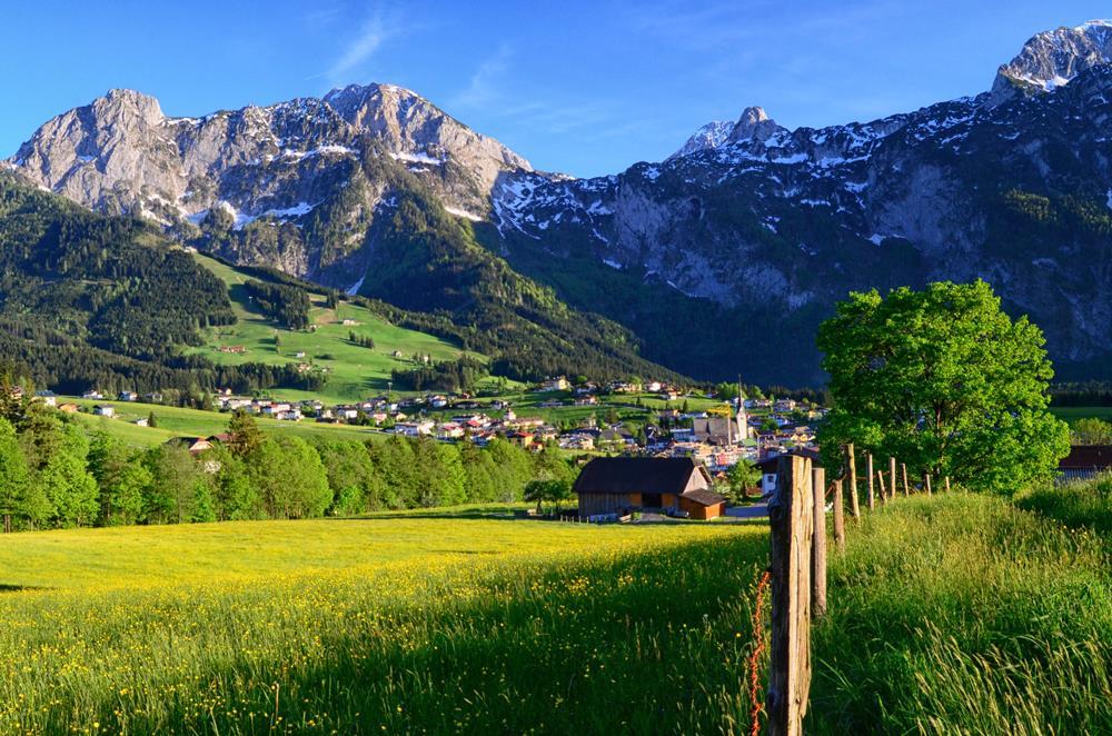 A picturesque mountain landscape with green meadows and a small town in the valley. The snow-capped peaks complete the idyllic picture.