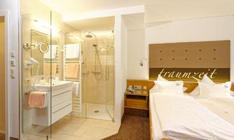 A modern hotel room with a comfortable bed and an elegant bathroom. The shower is separated by a glass wall and the overall picture radiates coziness.