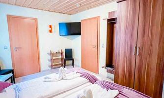 A cozy bedroom with two beds and a wooden ceiling. There is a television and a wardrobe, as well as doors leading to other rooms.