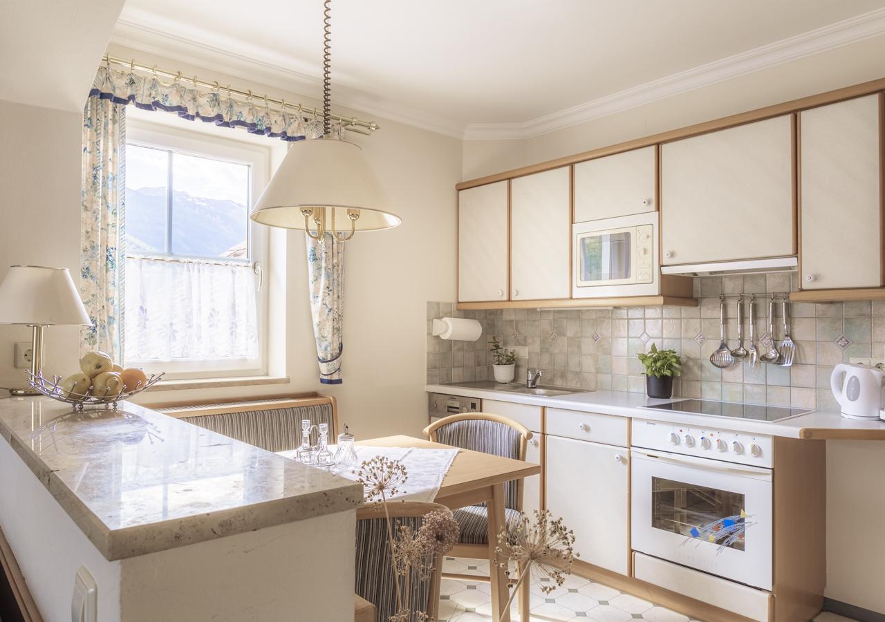 A bright kitchen with white cabinets and a cozy seating area. Large windows provide plenty of daylight and a friendly atmosphere.