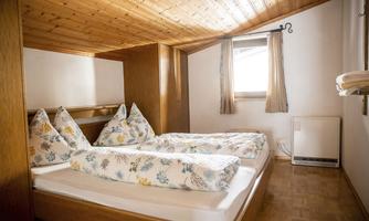 A cozy bedroom with two single beds and a wooden ceiling. The bedding features a floral design and a window provides daylight.
