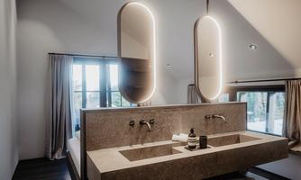 A modern bathroom with an elegant sink and two illuminated mirrors. Large windows let in plenty of daylight and create a relaxed atmosphere.