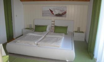 A modern bedroom with a large double bed and green pillows. There are bright walls and a warm wood ceiling, as well as discreet decor.