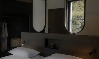 A modern bedroom with a double bed and large mirrors. The decor is minimalist and there is a window view.