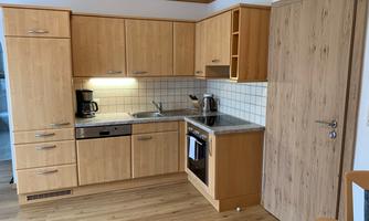 A modern wooden kitchen with white tiles and a stove. The kitchen layout is compact and functional.