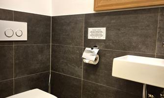 A modern bathroom with a toilet and a small sink. The walls are designed with gray tiles, and there is a mirror.