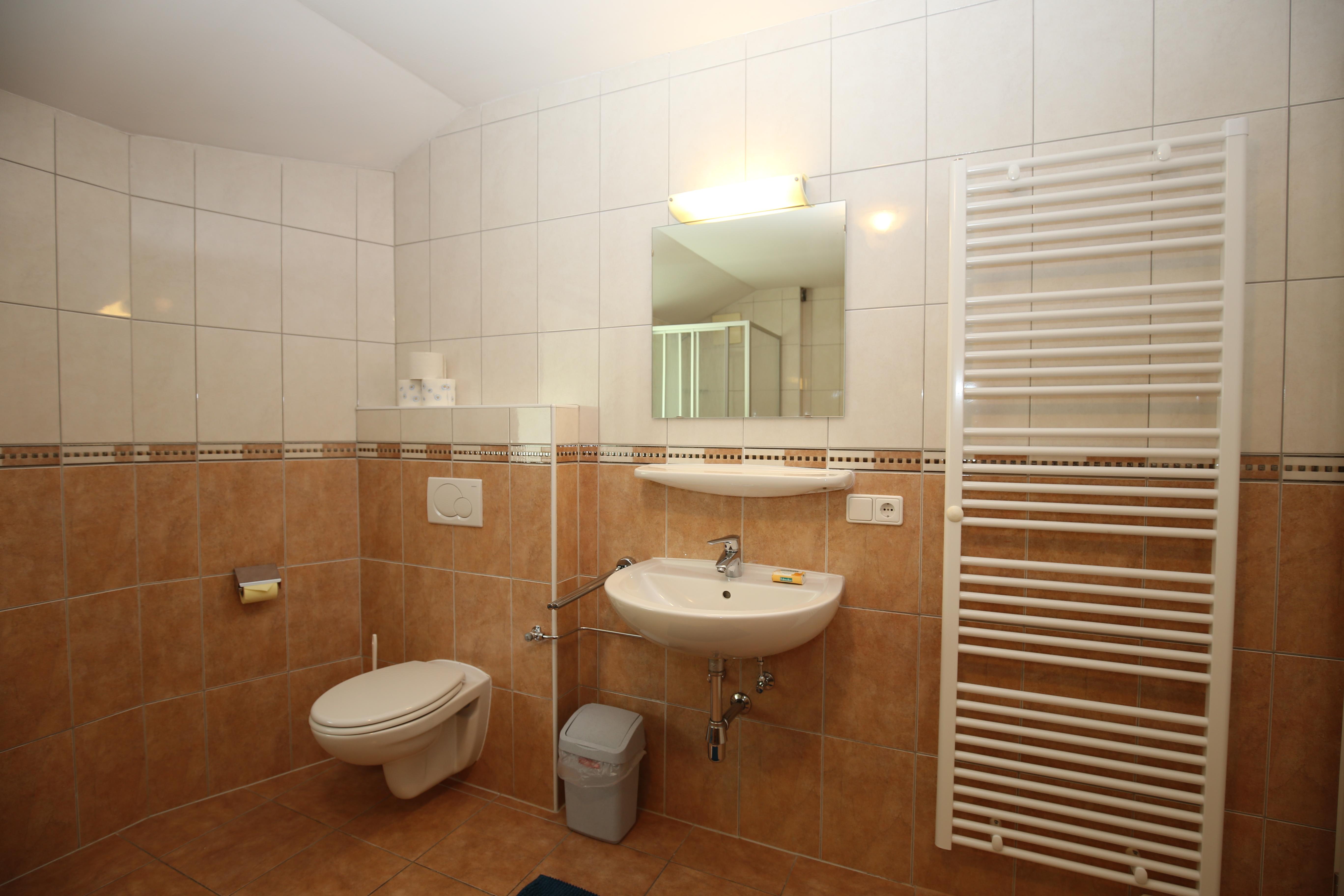 A modern bathroom with white tiles and brown accents. It features a sink, a toilet, and a towel warmer.