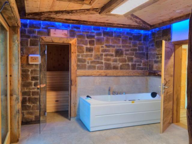 A modern bathroom with a white bathtub and blue LED lights. The walls are made of natural stone and there is a sauna.