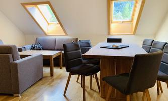 A modern living room with slanted ceilings and large windows. There is a dining table and cozy seating.
