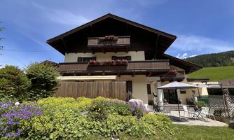The Sonnberg Lodge in summer, balconies and colorful flowers in the foreground. The sky is clear and the surroundings are green and inviting.