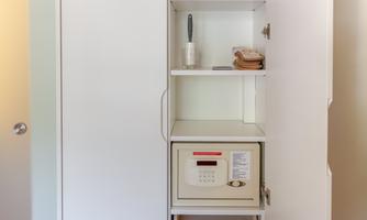 A white cabinet with a built-in safe and some shelves. On the shelves are a brush and a couple of towels.