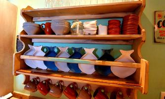 A wooden shelf with various pots and cups in vibrant colors. Glasses and dishes are neatly arranged at the top.